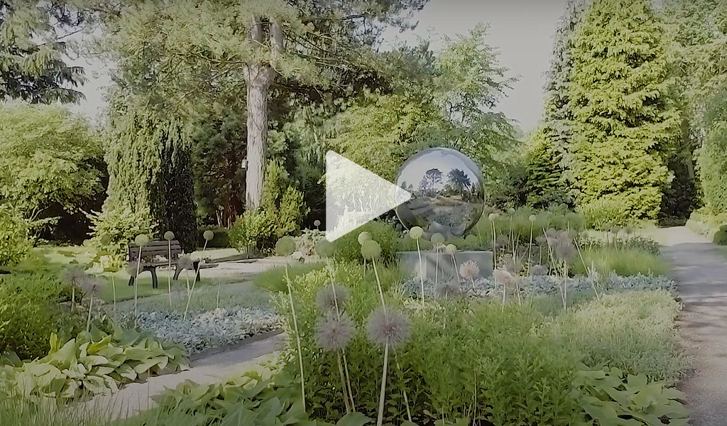 Friedhof mit Blumenbeeten und spiegelnde Weltkugel als Urne mit Weg und Bank in Pflanzen