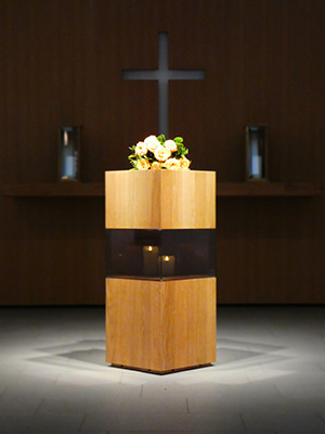 Urnenständer Ewiges Licht aus Holz mit Kranz und Kreuz im Hintergrund, Trauerfeier